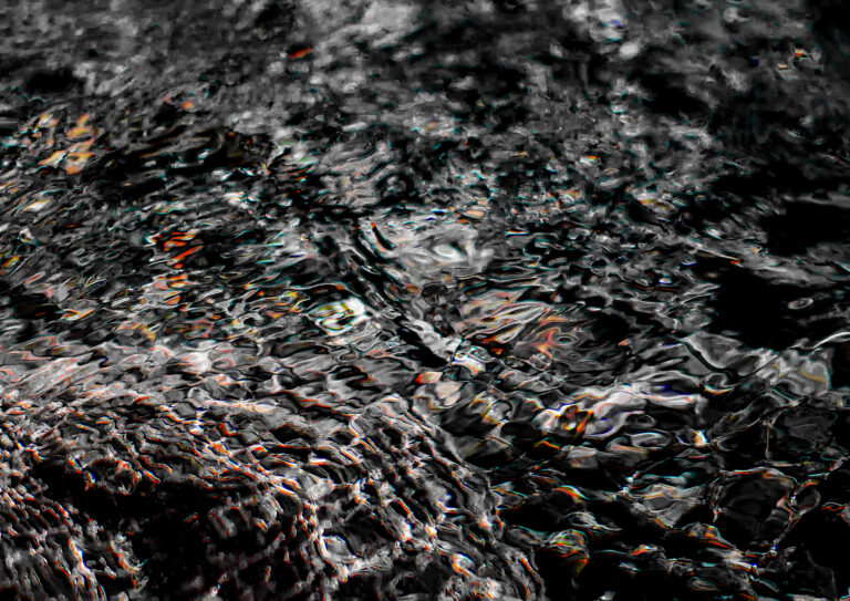 Close-up of dark rippling water with iridescent light reflections in black and white, abstract photography