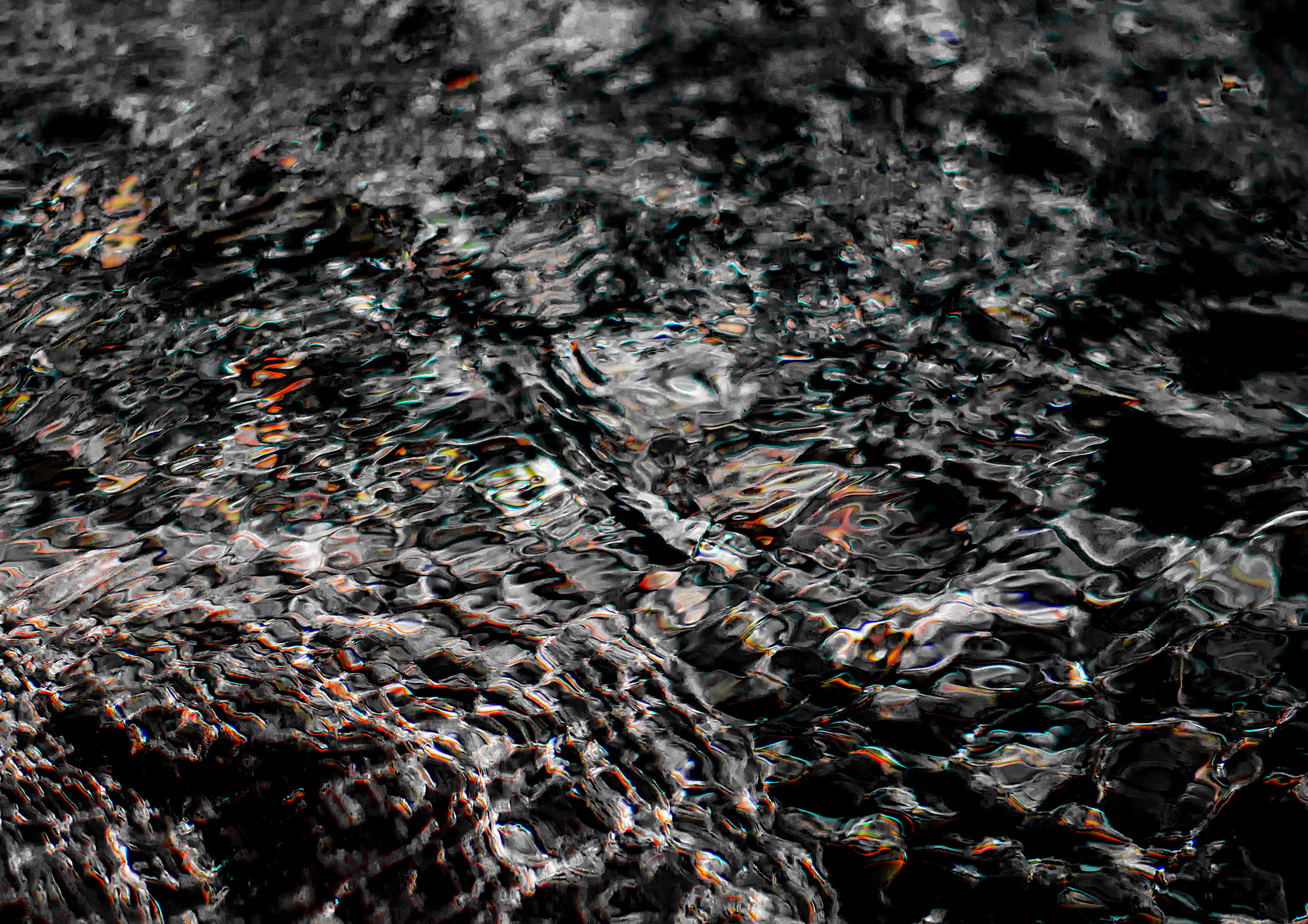 Close-up of dark rippling water with iridescent light reflections in black and white, abstract photography